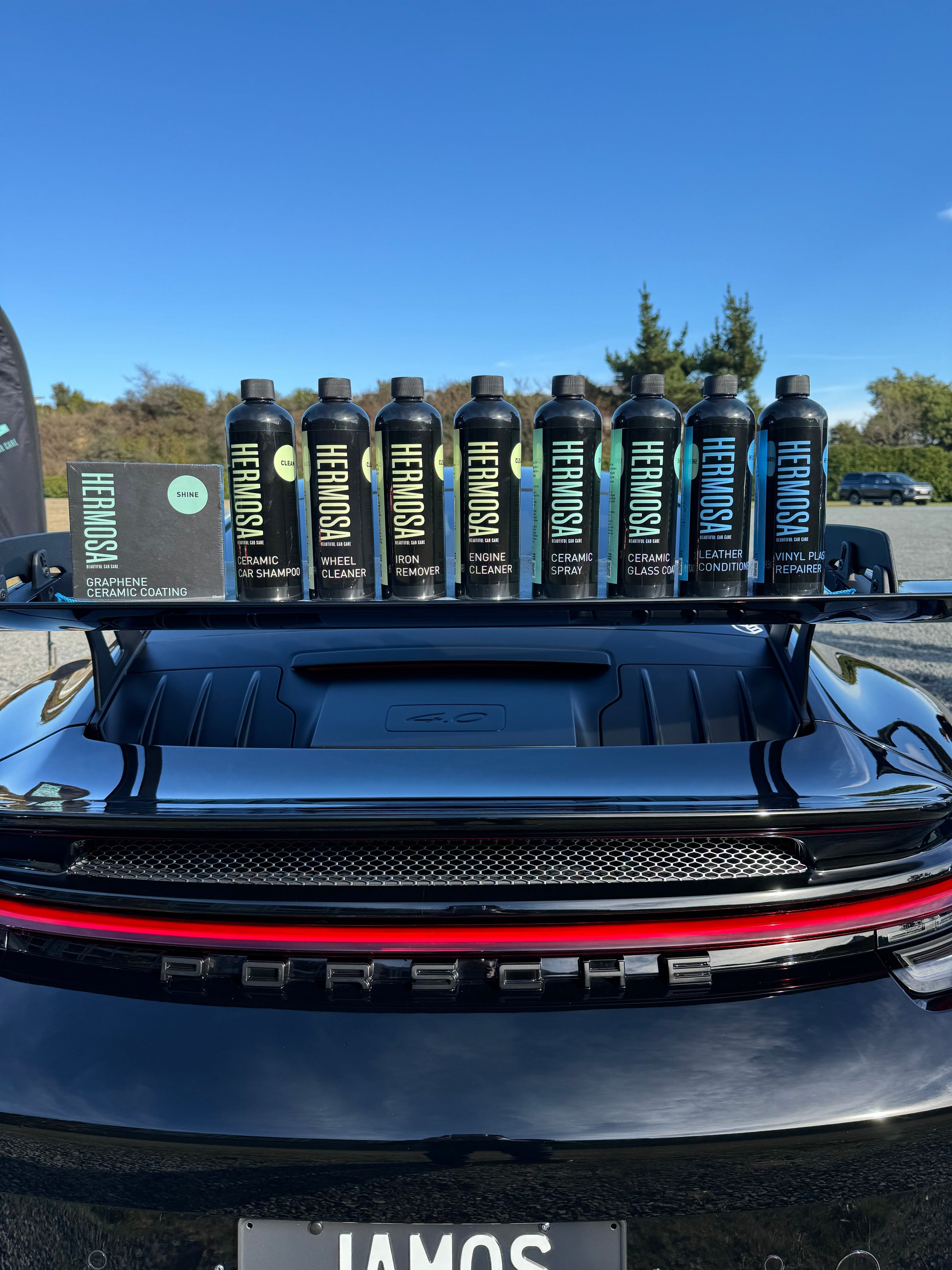 Hermosa car care products displayed on a Porsche trunk under blue skies.