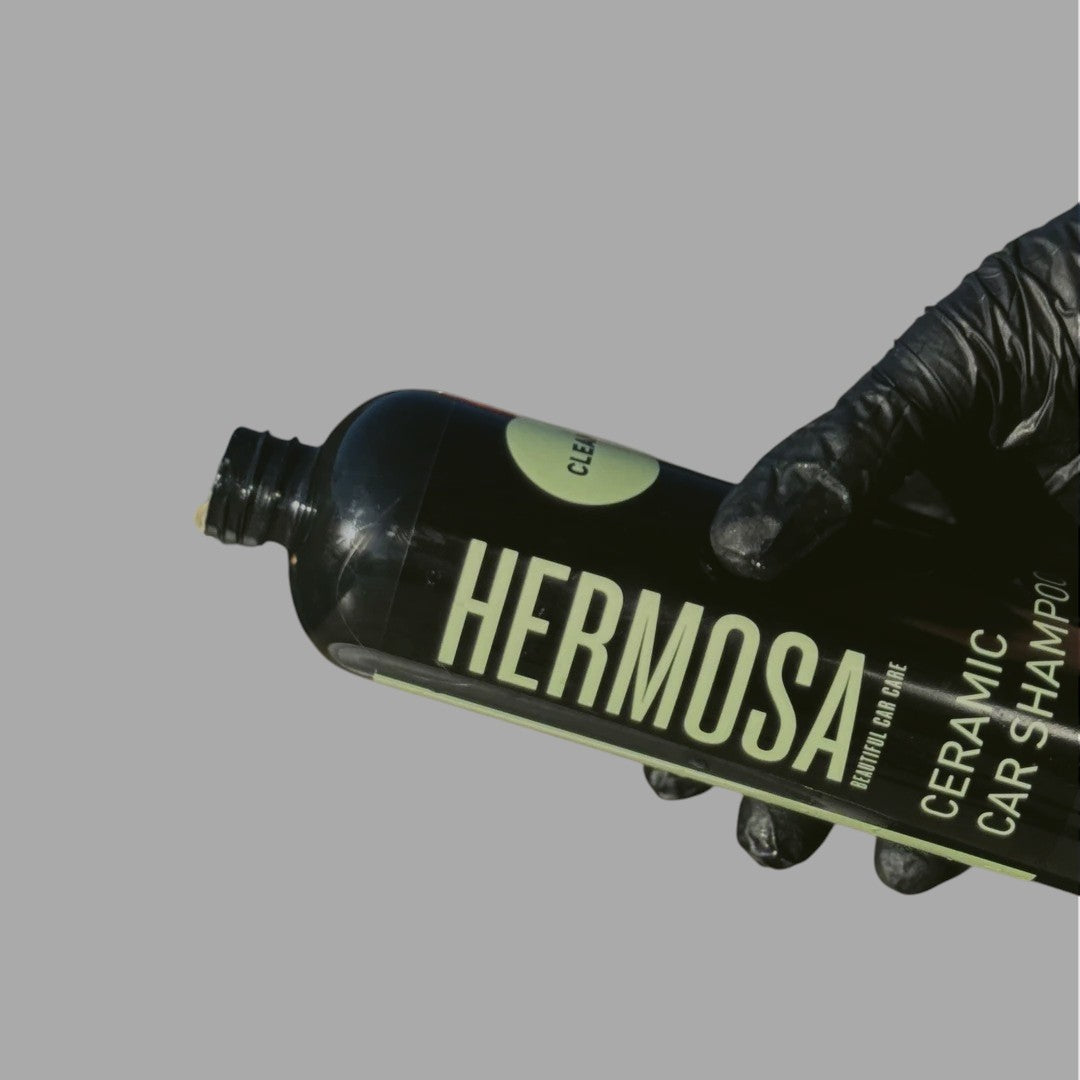 Person holding a bottle of Hermosa Ceramic Car Shampoo with black gloves.